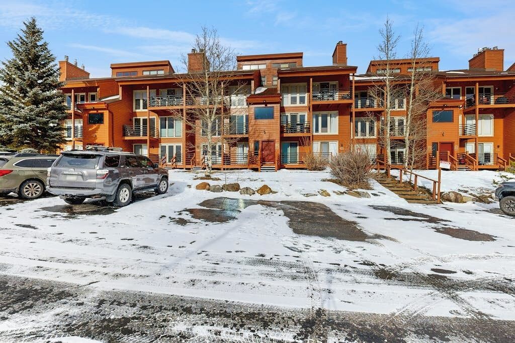 A multi-story building with balconies, a parking lot with cars, and a snowy ground.