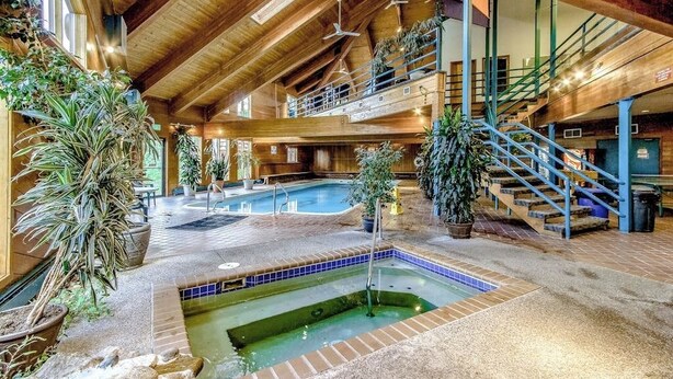 A spacious indoor pool area with multiple levels, wooden beams, and potted plants. - Cozy condo with fireplace, pool, & hot tub - near trails (Silverthorne)