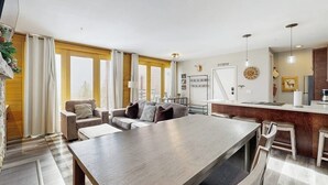 A modern living room with a dining table, sofas, and a kitchen area with a bar. - Cozy condo with fireplace, pool, & hot tub - near trails (Silverthorne)