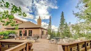 A wooden deck with outdoor furniture, a barbecue grill, and a building with a chimney in the background. - Cozy condo with fireplace, pool, & hot tub - near trails (Silverthorne)