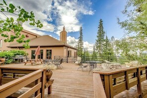 A wooden deck with outdoor furniture, a barbecue grill, and a building with a chimney in the background. - Cozy condo with fireplace, pool, & hot tub - near trails (Silverthorne)