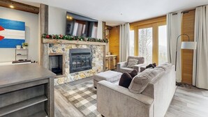 A modern living room with a stone fireplace, a sofa, a coffee table, and a TV mounted on the wall. - Cozy condo with fireplace, pool, & hot tub - near trails (Silverthorne)