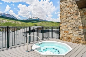 Ein Whirlpool auf einer Holzterrasse mit einer Steinmauer, einem Metallgeländer und Blick auf die Berge.