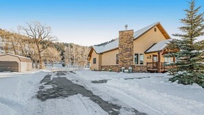 En snötäckt uppfart som leder till ett hus med en skorsten av sten, ett garage och ett snötäckt landskap.