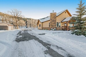 Ein verschneiter Weg führt zu einem Haus mit einem Steinofen, einer Garage und einer verschneiten Landschaft.