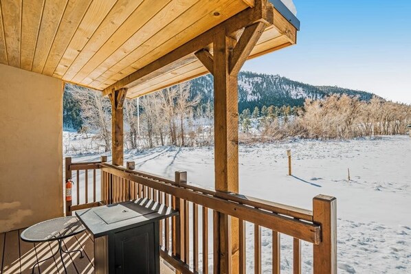 Eine Holzterrasse mit Tisch und Stühlen, mit Blick auf eine verschneite Landschaft mit Bäumen und Bergen.