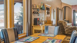 En ombonad inredning med ett matbord i trä, läderstolar, en kaffemaskin och en utsikt över snöklädda berg genom stora fönster.