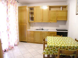 A small kitchen with wooden cabinets, a sink, and a table with a sunflower tablecloth. - Holiday apartment with air conditioning and terrace (Rosolina Mare)