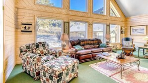 Une pièce chaleureuse avec des murs en bois, de grandes fenêtres, un canapé en cuir, un pouf à motifs et une table basse en bois.
