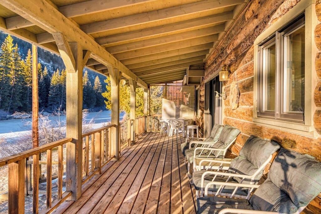 A wooden deck with chairs and a table, overlooking a forested area.