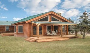 A log cabin with a porch, two chairs, and a small table. - Ranch-style main house with new barn and corral, set against the mountains (South Fork)