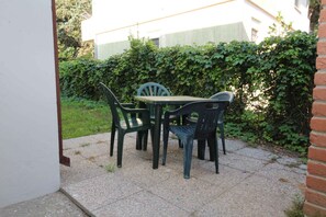 Eine Terrasse mit Tisch und Stühlen, eine Ziegelmauer und ein Hecken im Hintergrund.