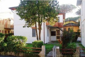 Ein Wohngebäude mit weißer Fassade, einem kleinen Vorgarten und einem Baum.