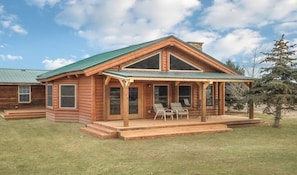 Eine Blockhütte mit Veranda, zwei Stühlen und einem kleinen Tisch.