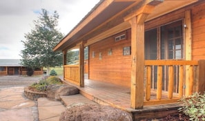 Eine Holzhütte mit Veranda, einem Steinweg und einem großen Baum im Hintergrund.