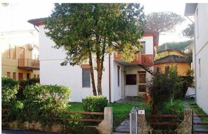 Ein Wohngebäude mit weißer Fassade, einem sichtbaren Balkon und einem Baum im Vordergrund.