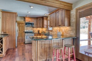 Eine Küche mit Holzausstattung, einer zentralen Kochinsel mit Hockern, einer Mikrowelle und einem Backofen.