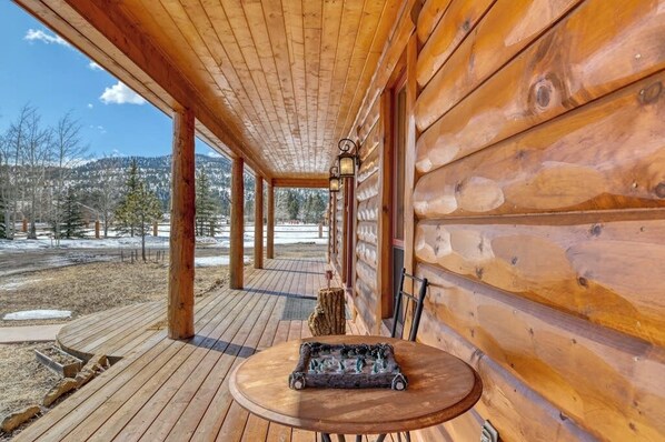 Eine Holzhütte mit einer Veranda, einem Tisch mit Schachbrett und Blick auf eine verschneite Landschaft.