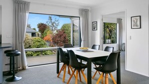 Un espace de repas moderne, avec une table et des chaises, de grandes fenêtres avec des rideaux et une vue sur l’extérieur.