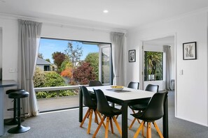 A modern dining area with a table and chairs, large windows with curtains, and a view of the outdoors. - Relax & Unwind Close to Lake & Town (Taupō)