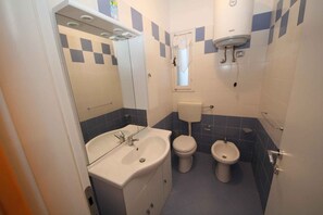 Ein Badezimmer mit Waschbecken, zwei Toiletten, einem Fenster und einem Warmwasserbereiter.