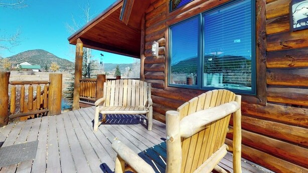 Eine Holzhütte mit einer Veranda, zwei Adirondack-Stühlen und einem großen Fenster.