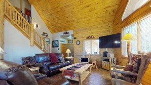 Ein Holzinterieur mit einem Ledersofa, einem Holztisch, einem Holzsesseln, einem Fernseher und einer Treppe.