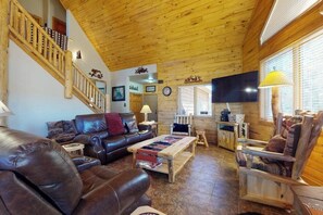 Ein Holzinterieur mit einem Ledersofa, einem Holztisch, einem Holzsesseln, einem Fernseher und einer Treppe.