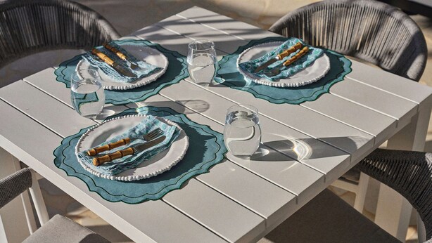 A table set with plates, cutlery, and glasses, surrounded by wicker chairs. - Brooman 10 - Self-Contained Cabin with Covered Deck (Mollymook)