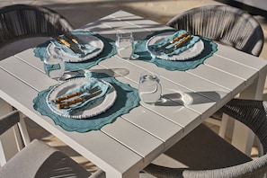 A table set with plates, cutlery, and glasses, surrounded by wicker chairs. - Brooman 10 - Self-Contained Cabin with Covered Deck (Mollymook)