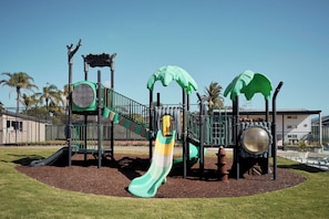A playground with slides, climbing structures, and a palm tree theme. - Brooman 10 - Self-Contained Cabin with Covered Deck (Mollymook)