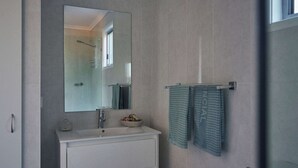 A modern bathroom with a large mirror, a sink, and a towel rack with two towels. - Brooman 10 - Self-Contained Cabin with Covered Deck (Mollymook)