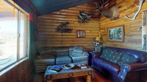 Ein rustikales Holzhäuschen-Interieur mit Holzbalkendecke, einem aufgehängten Hirschgeweih, einer Couch, einem Couchtisch und einem gerahmten Bild an der Wand.