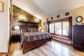 Ein Schlafzimmer mit Steinsandsteinwand, einem Bett mit gemusterten Betttextilien, einem Schmuckkästchen und einem Fenster mit Vorhängen.