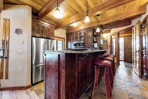 Eine Küche mit Holzausstattung, einem Edelstahlkühlschrank, einer Bar mit Hockern und einer Wanduhr.