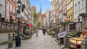 A cobblestone street lined with historic buildings, a church spire in the distance, and a market stall with jewelry. - Długa Grobla 10 by Grand Apartments (Gdańsk)