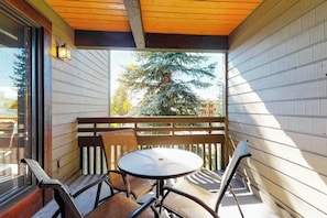 Ein Holzbalkon mit rundem Tisch und Stühlen, Blick auf einen Baum und ein Gebäude im Hintergrund.