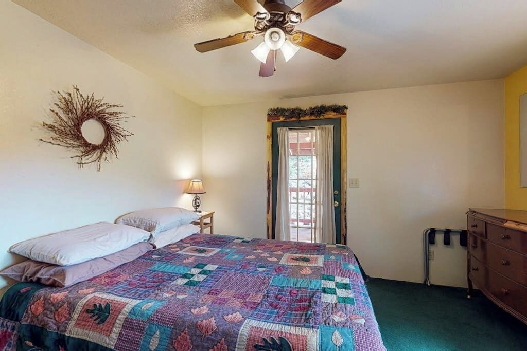Un dormitorio con cama, ventilador de techo, puerta con cortinas, cómoda y decoración en la pared.