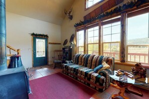 A cozy living room with a patterned sofa, a wooden staircase, and a large window with a view. - Charming rural cabin w/ mountain views, sauna, and deck - close to Rio Grande (South Fork)