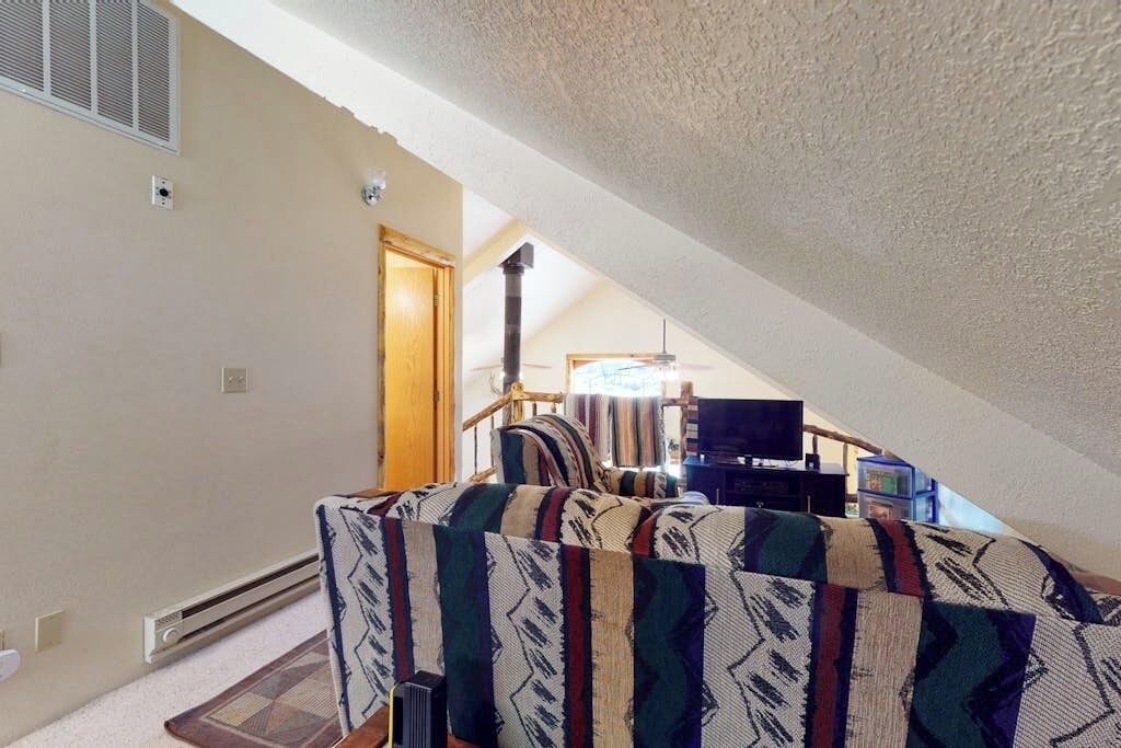 An attic room with a sloped ceiling, a built-in heater, a television, and a patterned sofa.