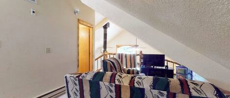An attic room with a sloped ceiling, a built-in heater, a television, and a patterned sofa.