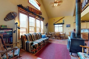 A cozy living room with a sofa, a fireplace, a dining area, and a bookshelf. - Charming rural cabin w/ mountain views, sauna, and deck - close to Rio Grande (South Fork)