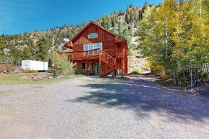 A two-story log cabin with a porch and a satellite dish, surrounded by a gravel driveway and autumn foliage. - Charming rural cabin w/ mountain views, sauna, and deck - close to Rio Grande (South Fork)