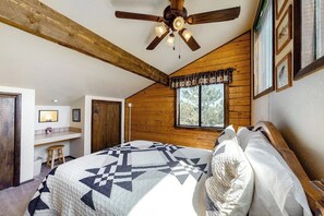 Ein Schlafzimmer mit Bett, Deckenventilator, Holzwänden, einem Fenster und einem kleinen Schreibtisch mit Stuhl.