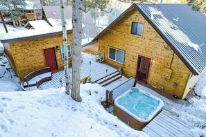 Eine Holzhütte mit Whirlpool, roter Tür und einer Terrasse.