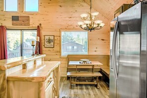 Ein Holzblockhaus-Interieur mit Küchenzeile, einer Bank, einer Kandelaberleuchte und einem Kühlschrank.