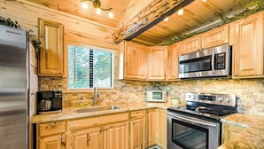 A kitchen with wooden cabinets, a stainless steel refrigerator, a microwave, a stove, and a window with blinds. - Near Town W/ Scenic Deck, Hot tub, Free WiFi, Full Kitchen & More (South Fork)