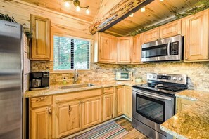 Eine Küche mit Holzausstattung, einem Edelstahl-Kühlschrank, einer Mikrowelle, einem Herd und einem Fenster mit Jalousien.