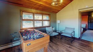 Quarto com teto de madeira, mesa de futebol de apoio, janela com vista e uma cadeira.