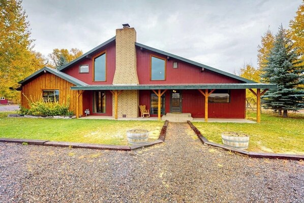 A two-story house with a red exterior, a brick chimney, and a covered porch. - Mountain View Home w/ jetted tub, air hockey, foosball near Wolf Creek (Del Norte)